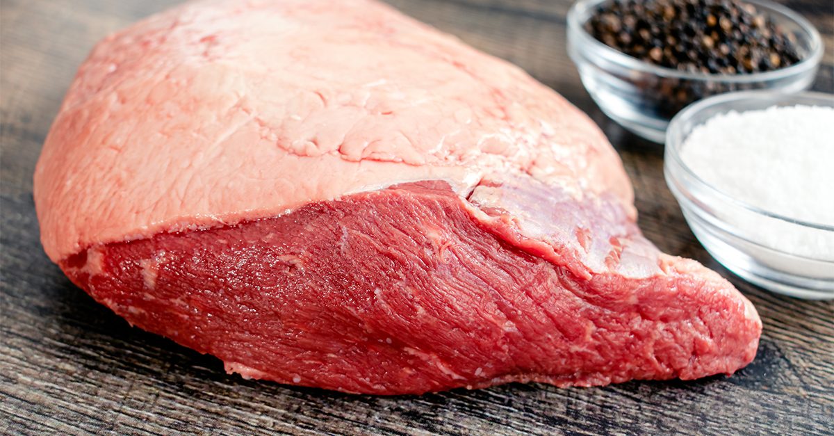 Uncooked beef rump with salt and pepper blurred in the background